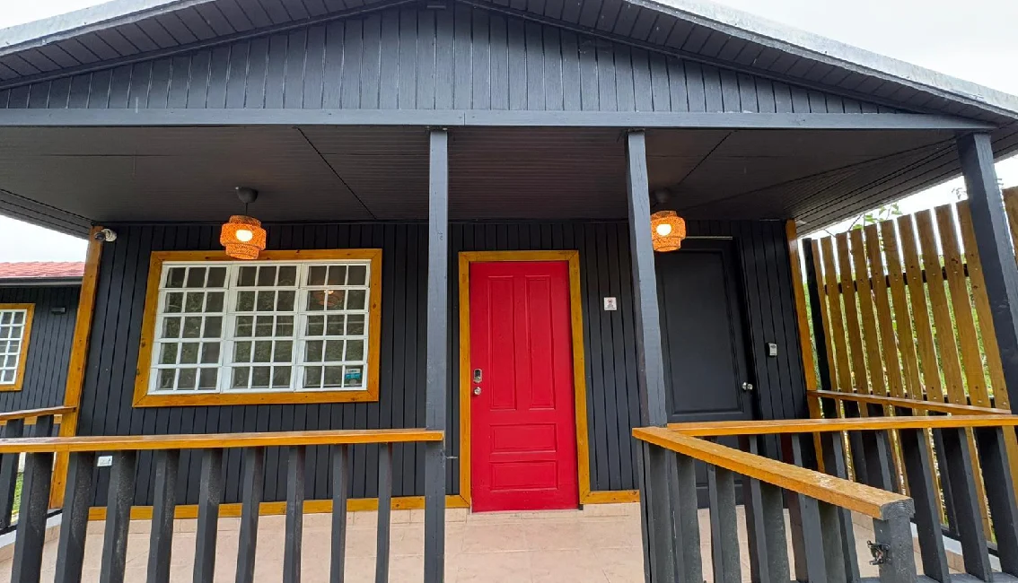 Front porch of a Naranjito Airbnb with black exterior walls, wood trim, railing, and red entrance door.